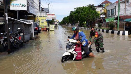 Seorang personel TNI membantu mendorong motor warga yang macet akibat banjir. (Ist)